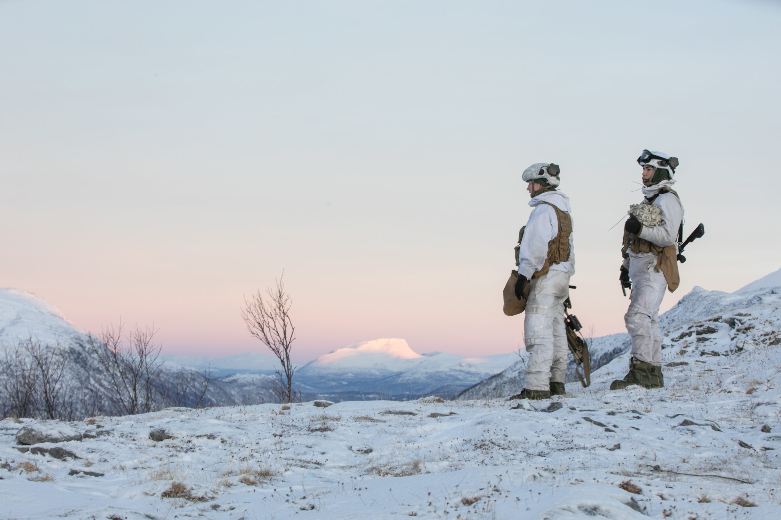 To soldater kledd i vinteruniform ser utover snødekt landskap.