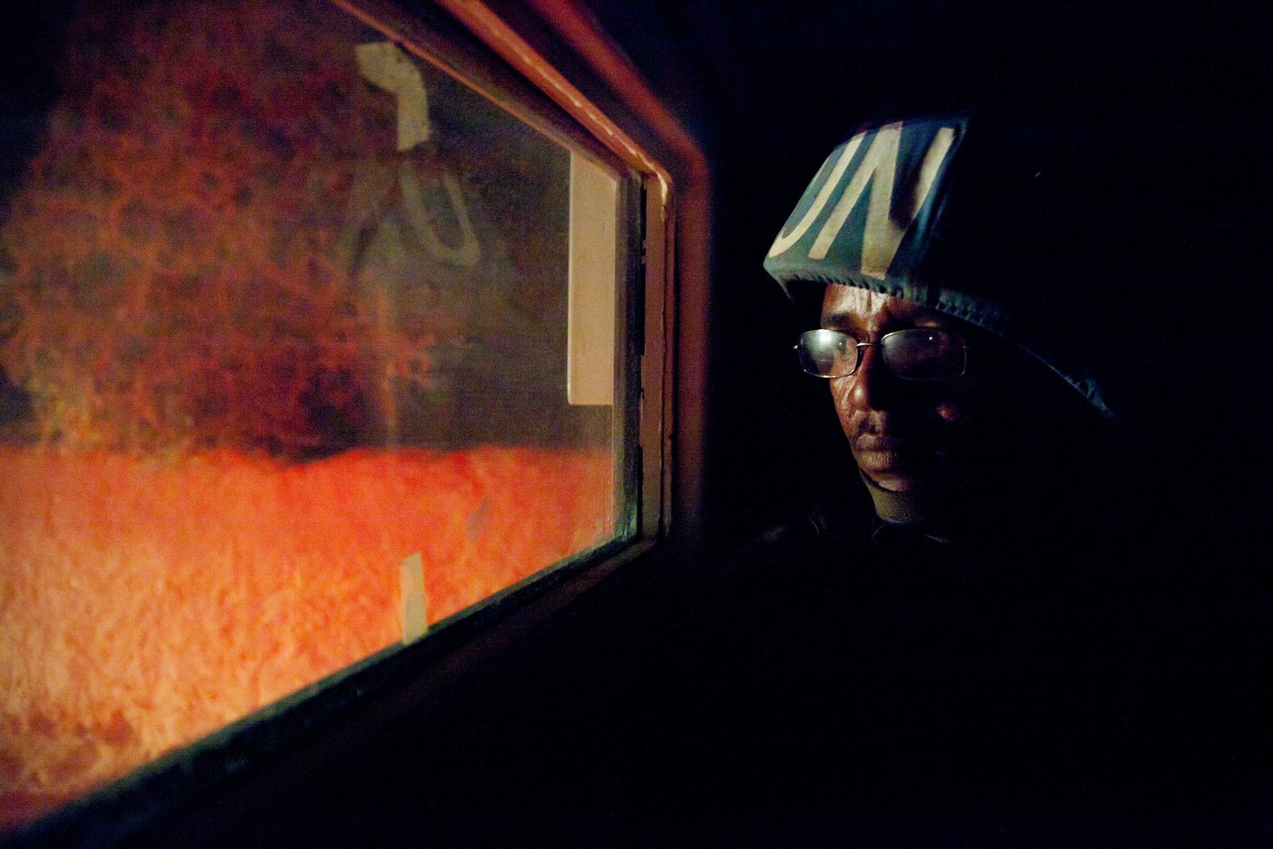 En mann med hjelm hvor det står UN, ser ut av et smalt vindu. Det er natt