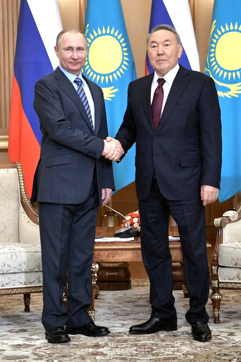 Putin og Nazarbayev tar hverandre i hendene foran en rekke med russiske og kasakhstanske flagg
