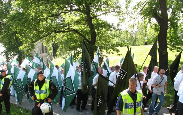 Medlemmer fra den nynazistiske grupperingen "Den nordiske motstandsbevegelsen" holder flagg med gruppens logo. Medlemmene er kledd i uniform.