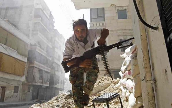 En mann med våpen løper i ruinene av en syrisk by.