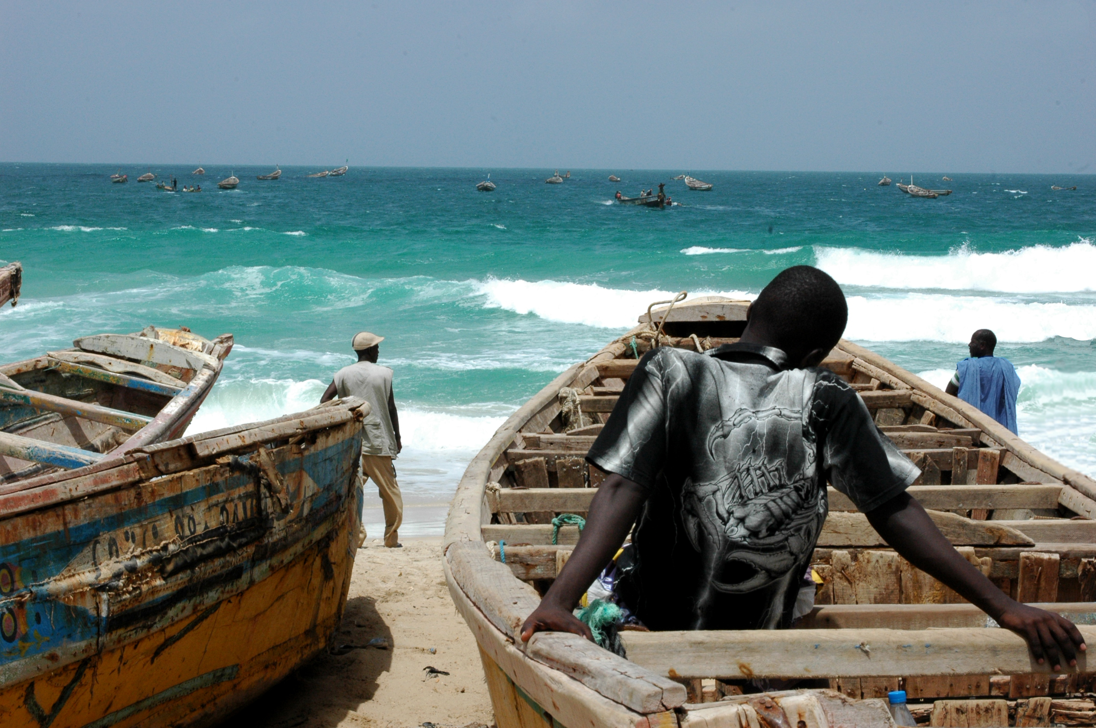 Ung mann sitter oppi en båt på land, ryggen til kamera, ser ut på havet 