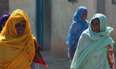 Eritreiske kvinner i gul, mintgrønn og blå kjoler går på gaten