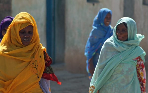 Eritreiske kvinner i gul, mintgrønn og blå kjoler går på gaten