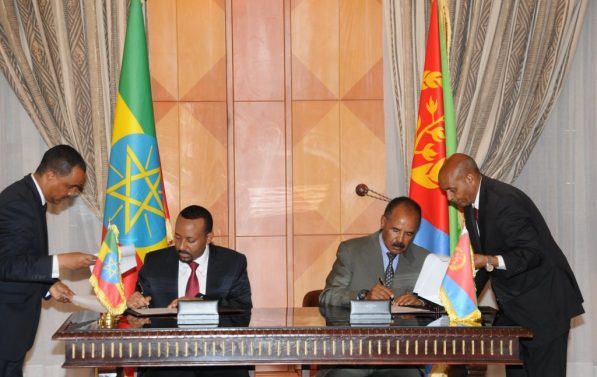 Abiy Ahmen og Isaias Afewerk sitter på enden av hvert sitt bord og skriver under på papirer