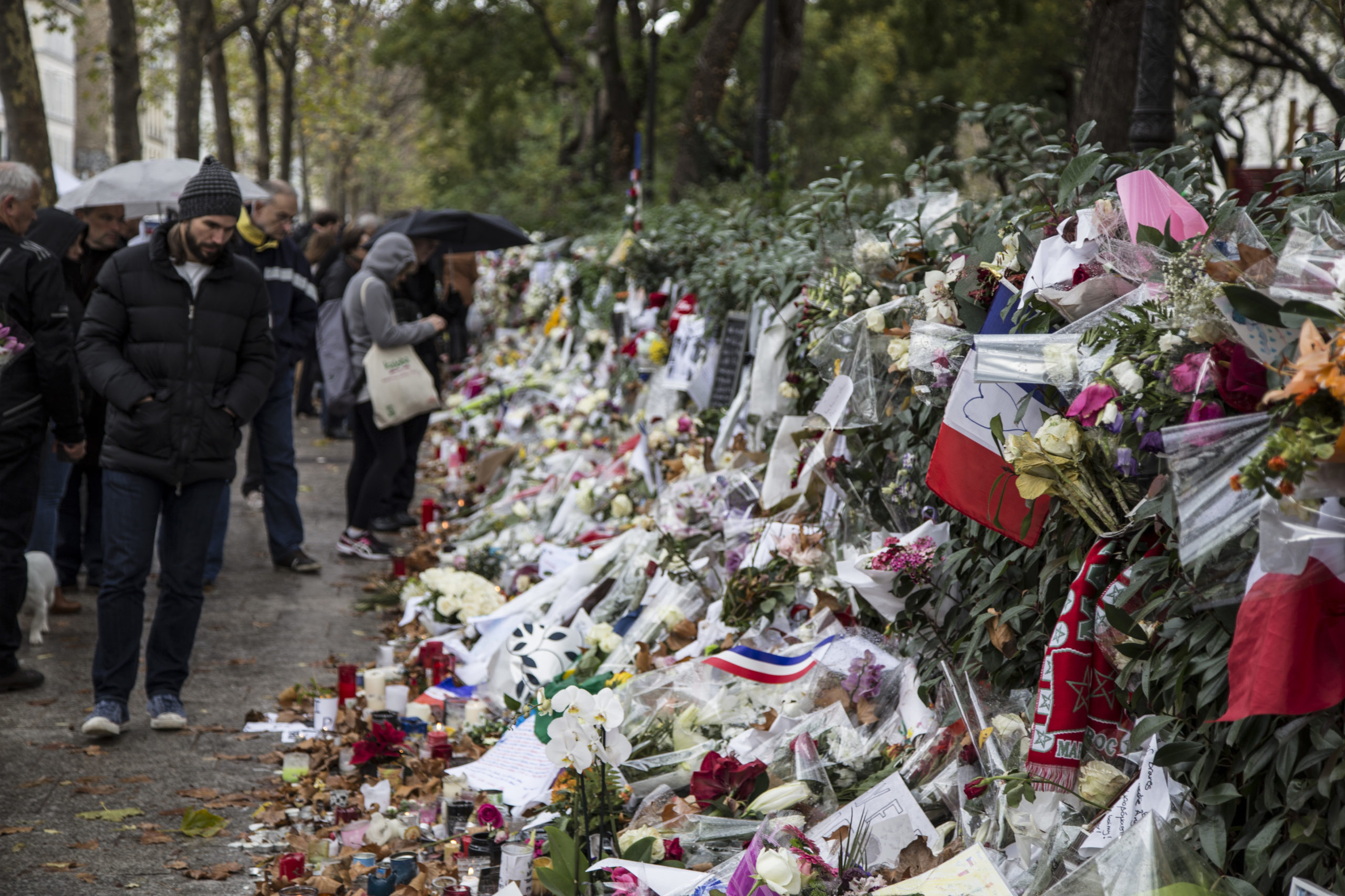 Lys, tegninger, flagg og blomster til minne om terrorofrene etter angrepene i Paris. Personer ser på.