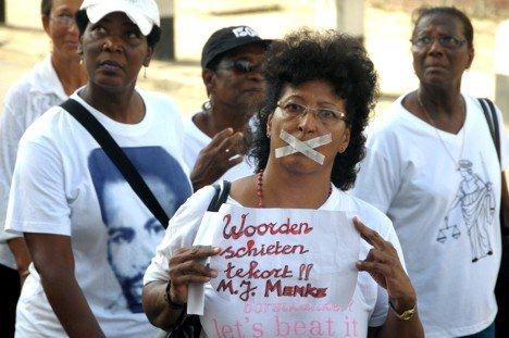 En kvinner går i demonstrasjonstog. Hun har teipet munnen og holder en plakat.