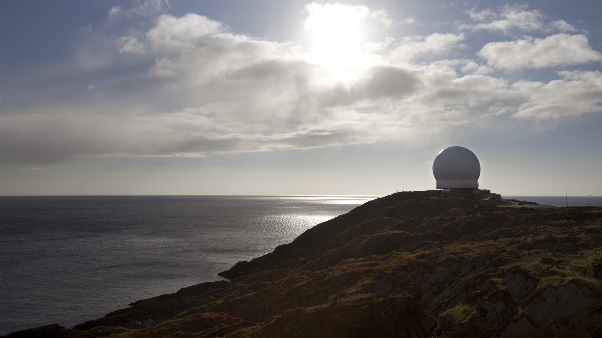 En globus formet radar står på en skrent med sjøen i bakgrunnen.