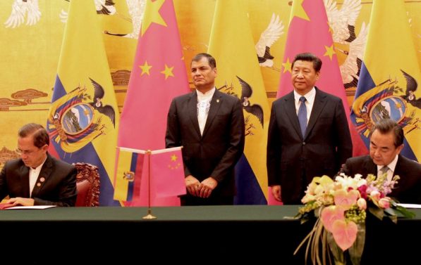 Ecuadors president Rafael Correa med kinas president Xi Jinping under statsbesøk i Kina. Bak dem er det flagg. To menn signerer, to menn står.