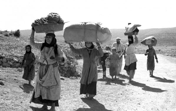 Kvinner og barn med sine eiendeler bært på hodet går langs en øde vei.