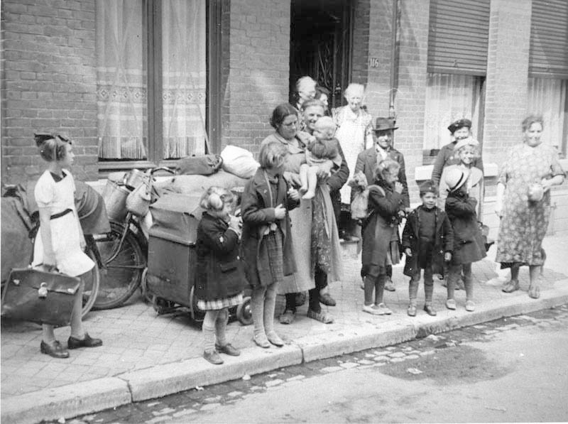 En storfamilie venter langs fortauet med alle sine eiendeler samlet bak seg.