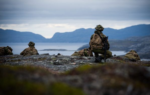 Noen soldater sitter på en topp med utsikt over en fjord.
