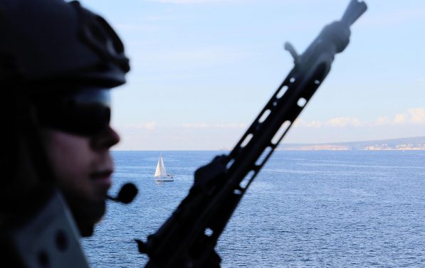 soldat med hjelm og våpen på skip, middelhavet i bakgrunnen