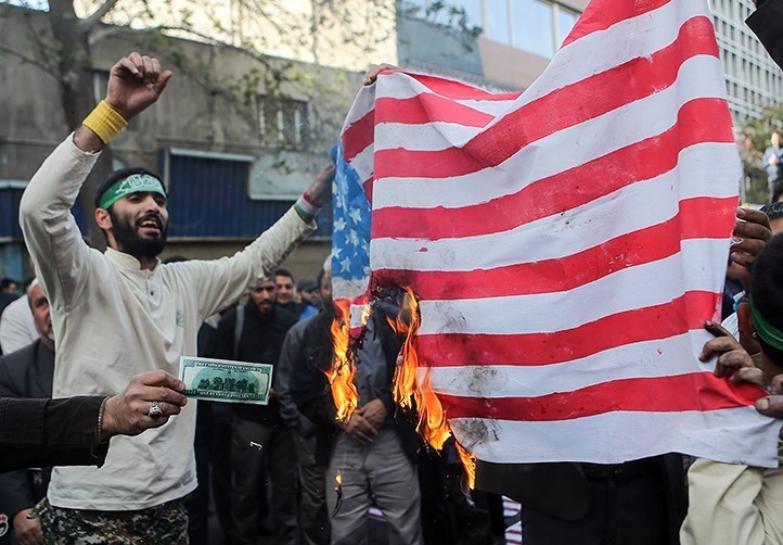 Folkemengde samlet rundt et amerikansk flagg som er satt fyr på.