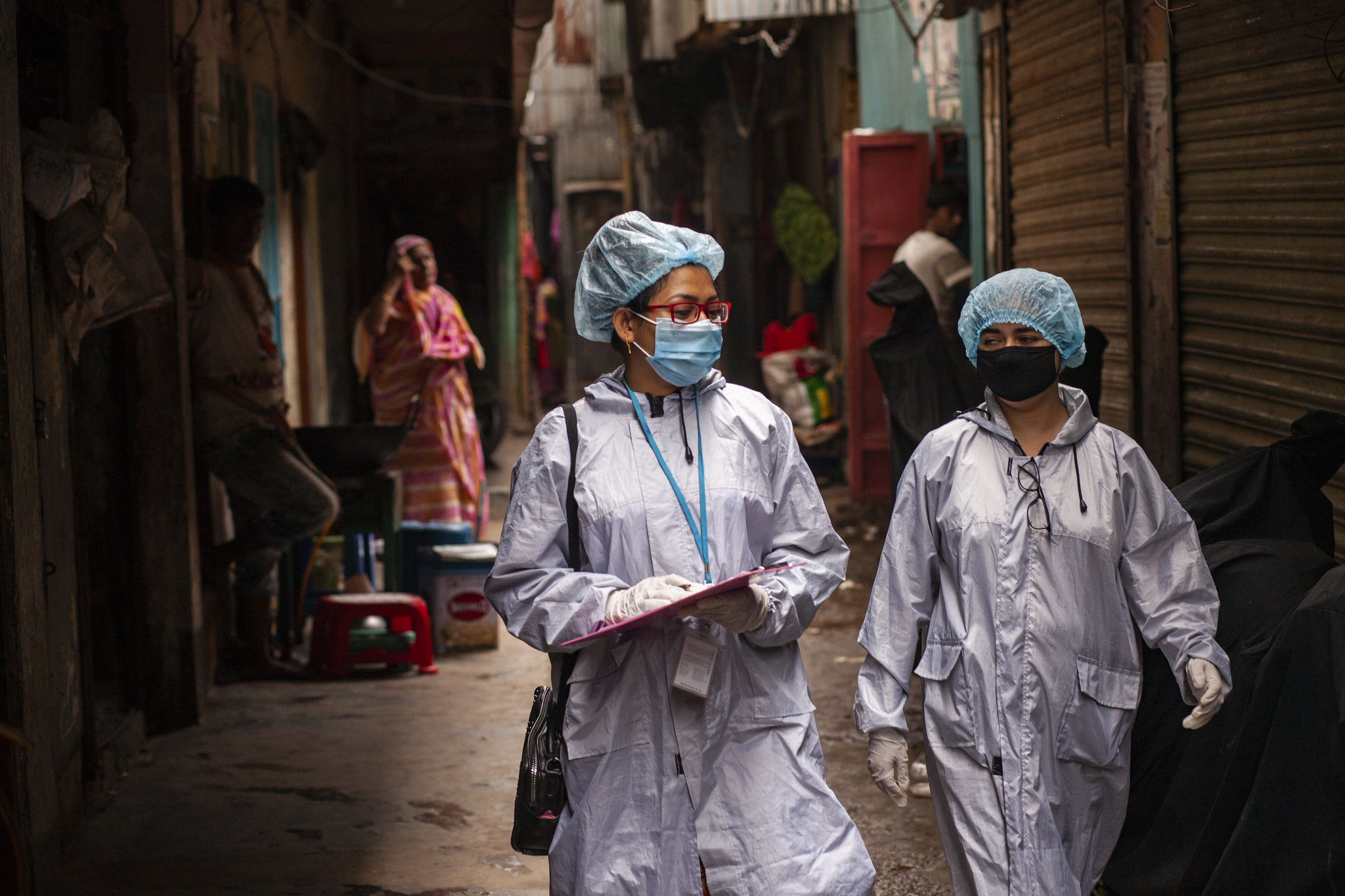 To kvinner kledd i smitteverneutstyr går gjennom en gate.