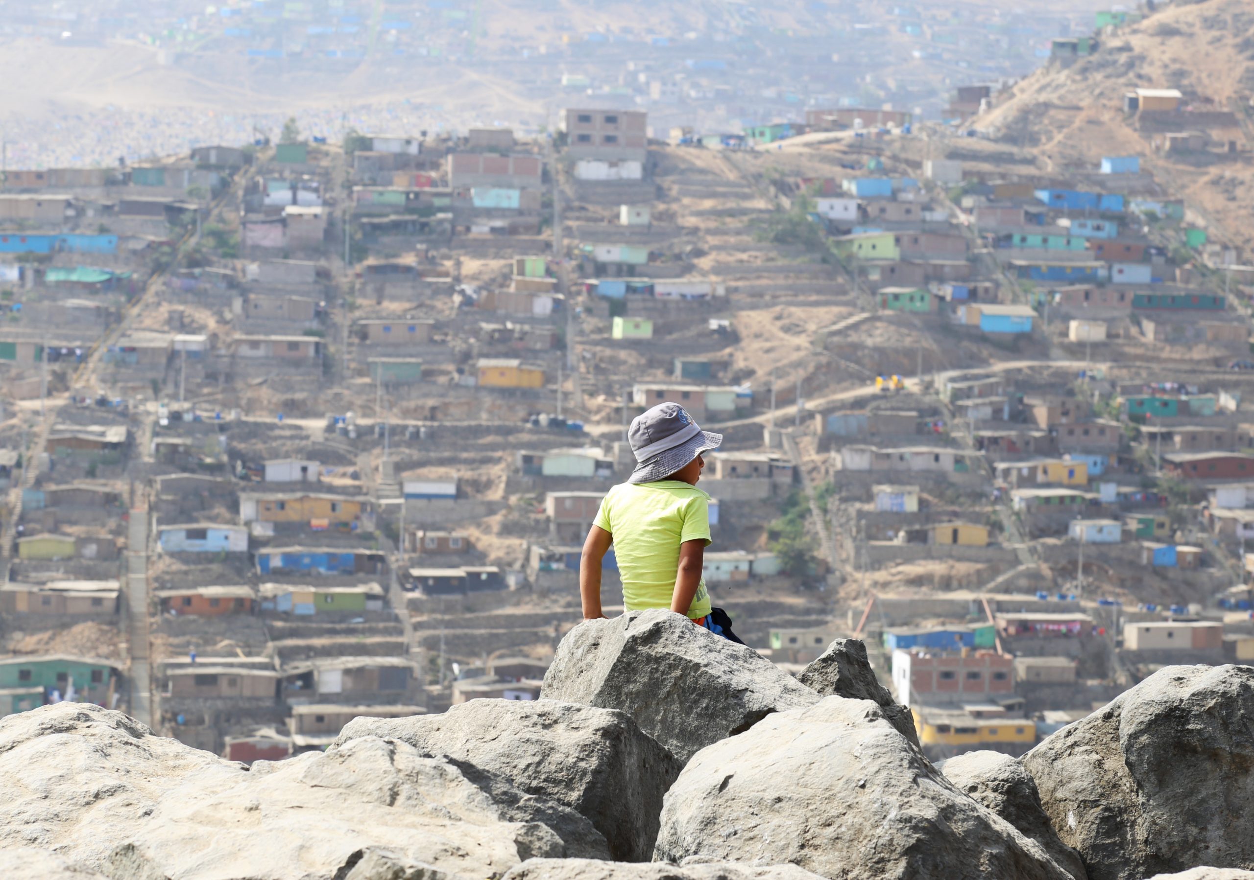 Et barn sitter på en klippe på et fjell og ser utover byen