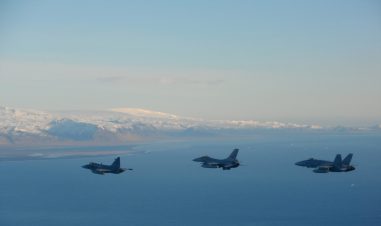 Tre jagerfly i formasjon over havet med snøkledde fjell i bakgrunnen.