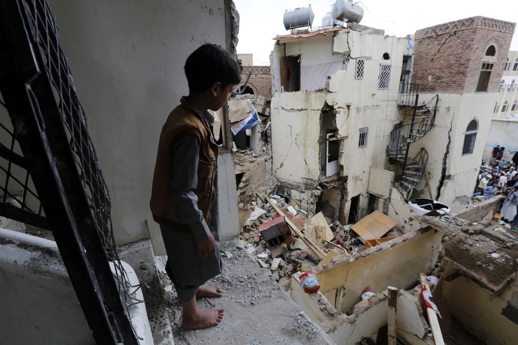 En gutt står i et utbombet hus og ser på ødeleggelsen utenfor.