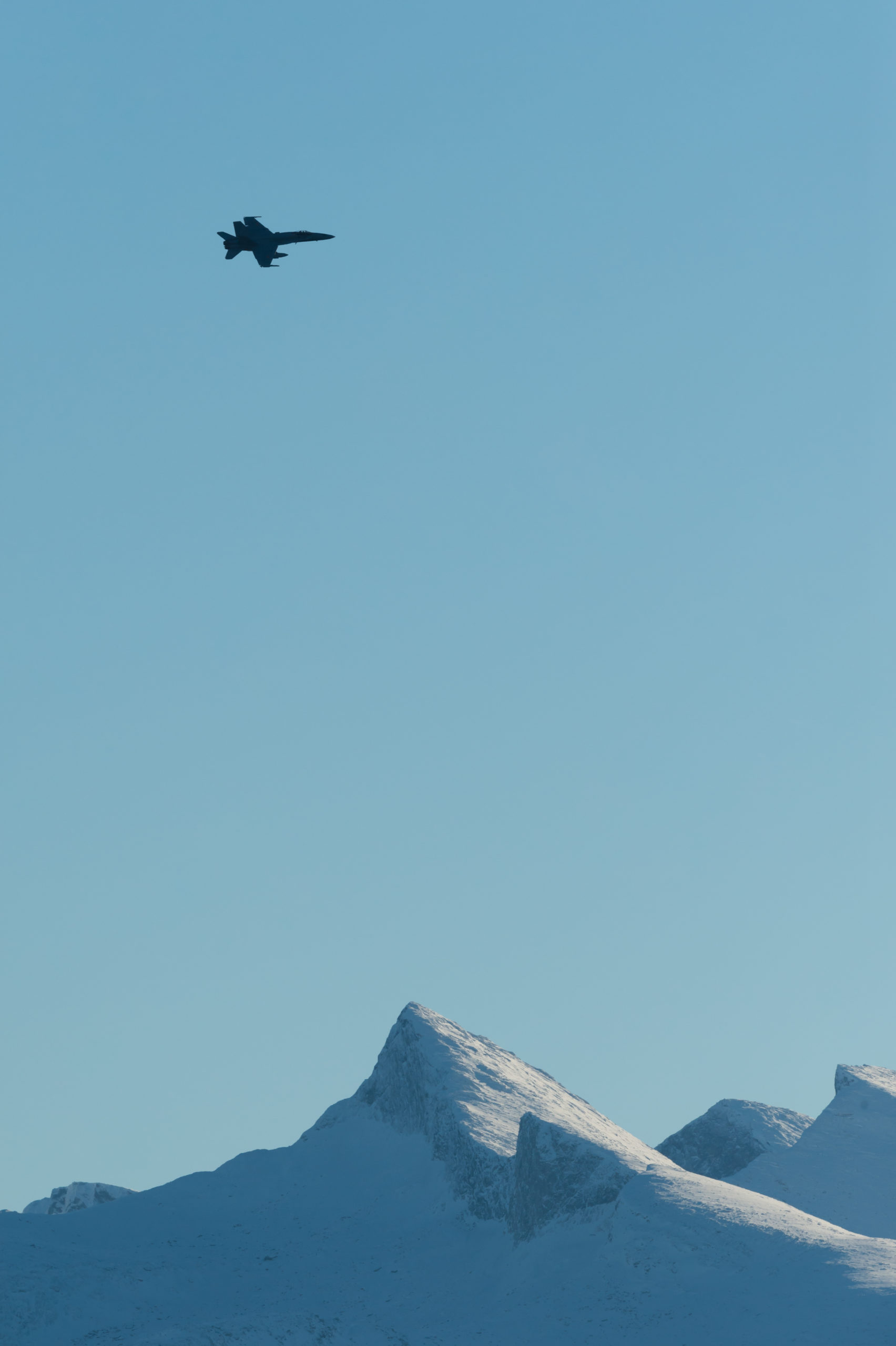 Et jagerfly i lufta over et snødekt fjell.