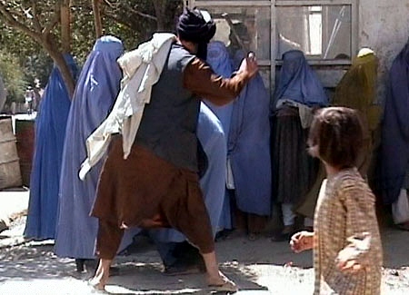 En mann fra Taliban slår en gruppe damer med en stokk, mens et barn ser på