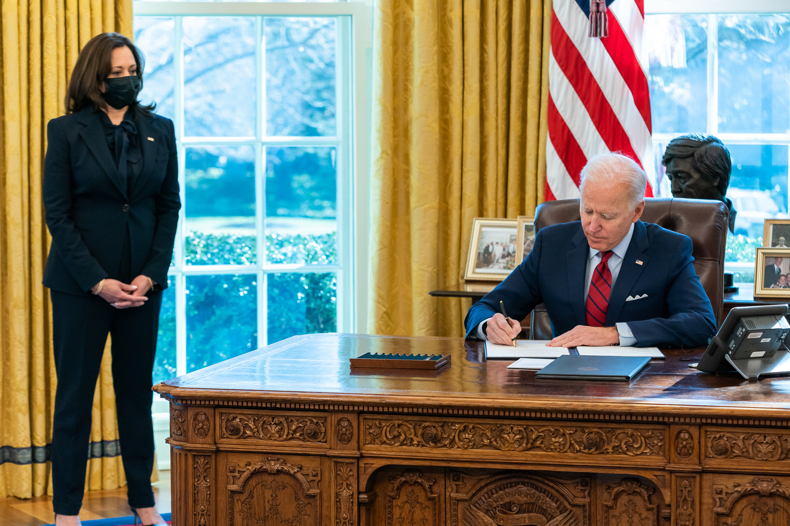 Joe Biden underskriver et dokument inne på Det ovale kontor med visepresident Kamala Harris til stede