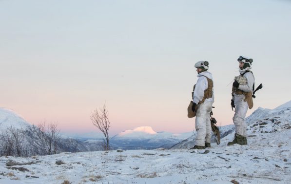To soldater kledd i vinteruniform ser utover snødekt landskap.