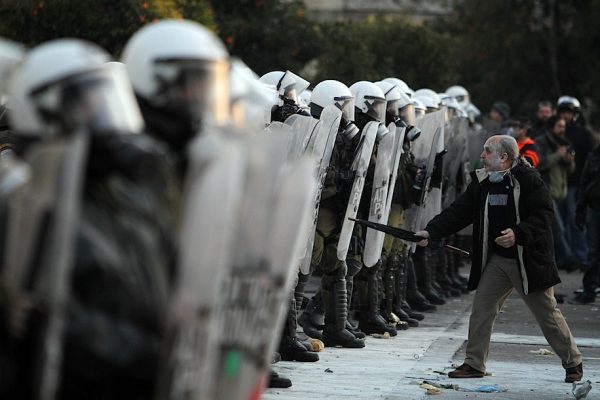 En mann står alene foran en lang rekke væpnet opprørspoliti.