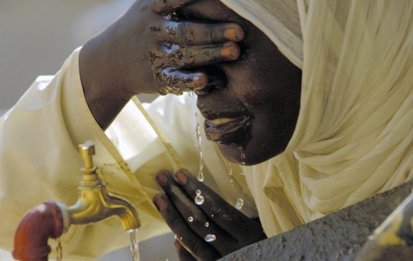 En kvinne vasker ansiktet sitt i vann fra en tappekran.