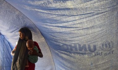 En kvinne med et lite barn på armen står inne i et UNHCR telt.