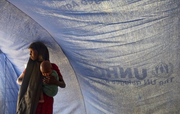 En kvinne med et lite barn på armen står inne i et UNHCR telt.