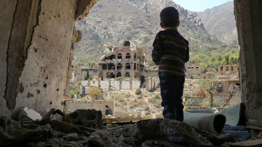 EN liten gutt står i ruinene av en bygning og ser ut.