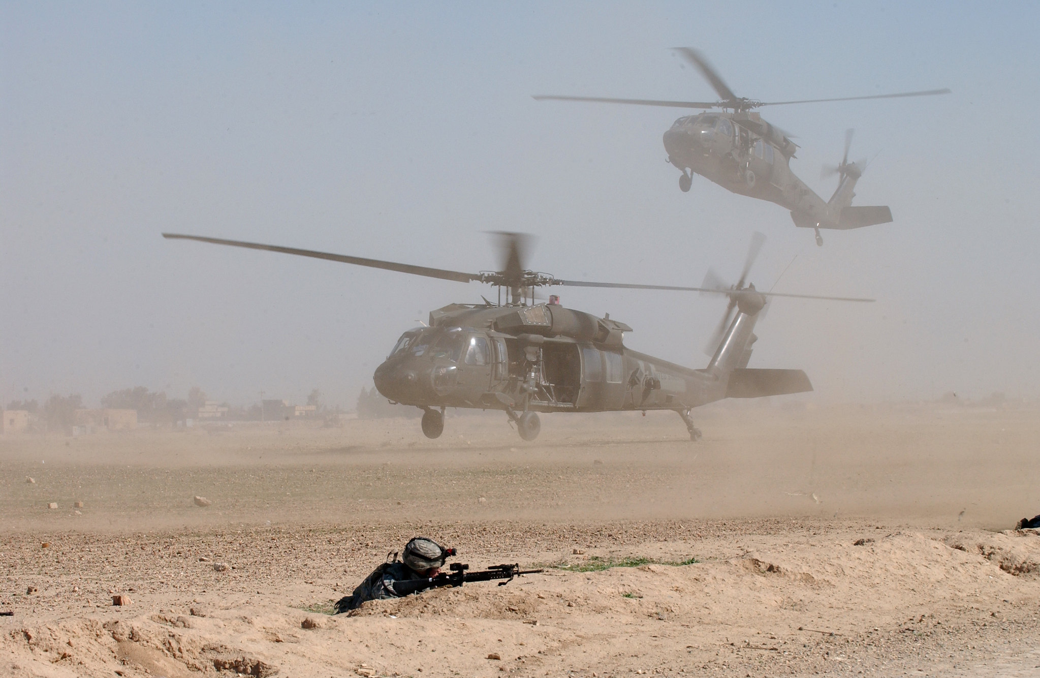 Soldat prøver å unngå sandskyen som piskes opp av to helikoptre som lander.