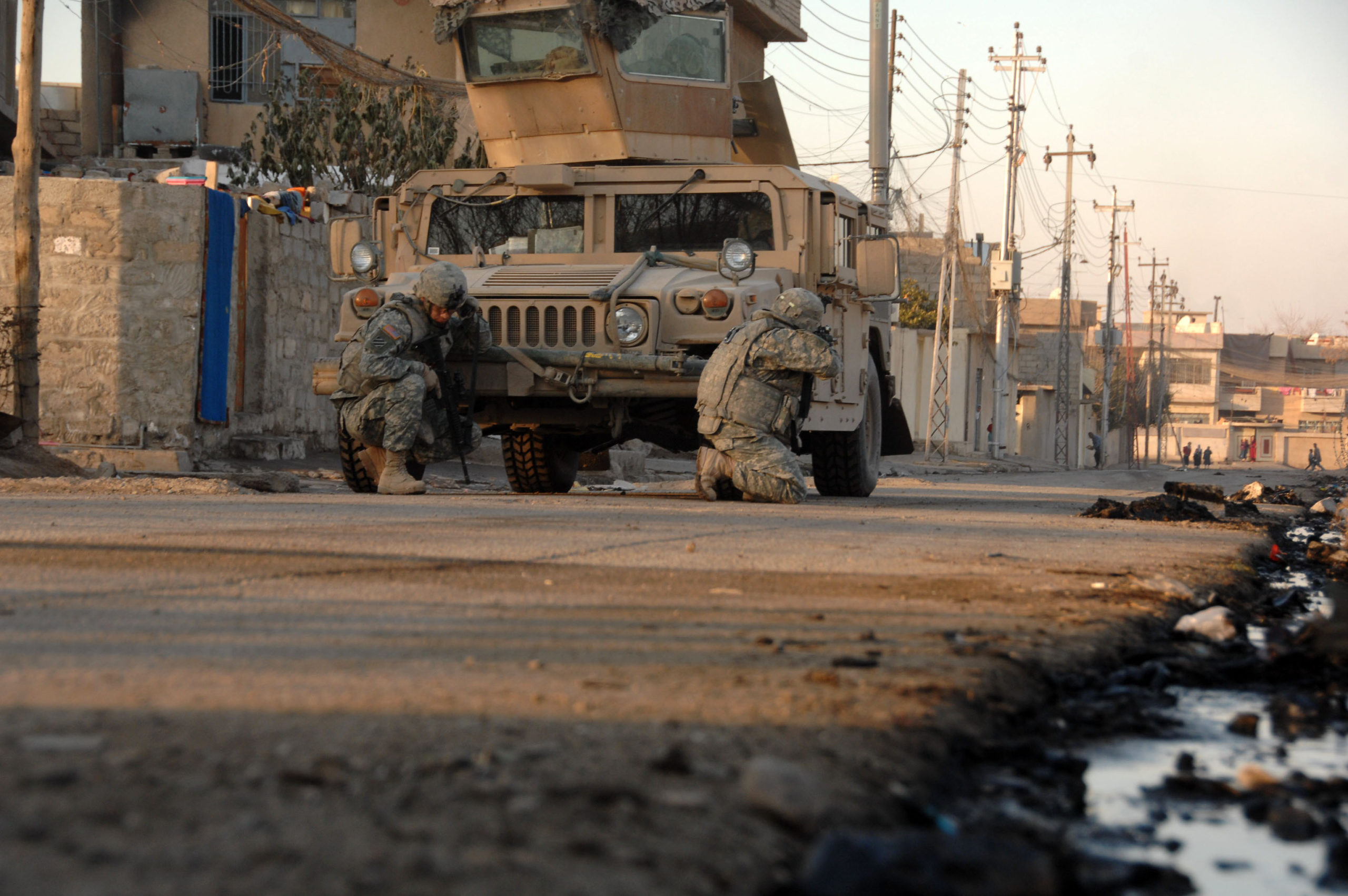 To soldater sitter i skjul av et militært kjøretøy.