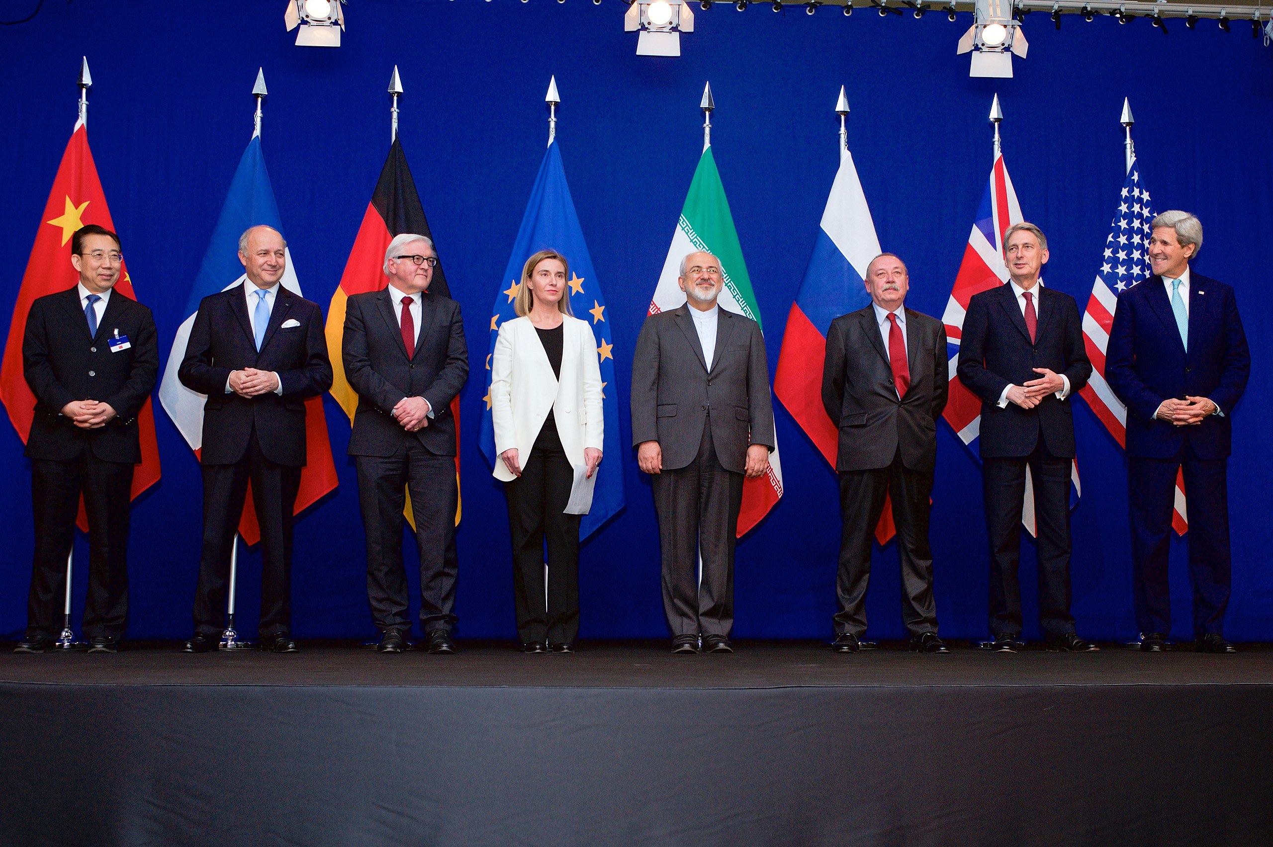 En rekke utenriksministere står foran sine lands flagg på en scene.