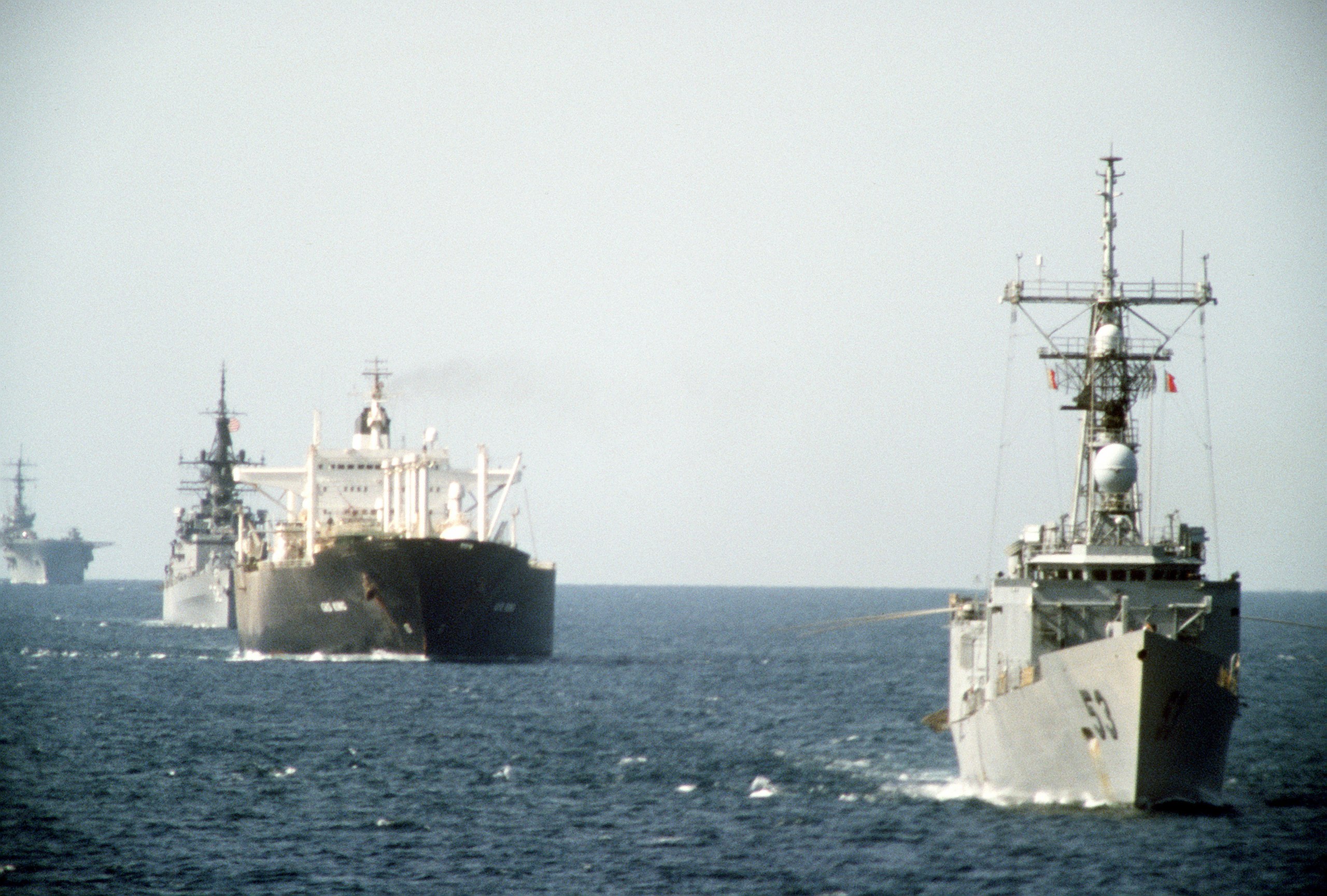 Militært skip i forgrunnen, etterfulgt av et sivilt og flere militære.