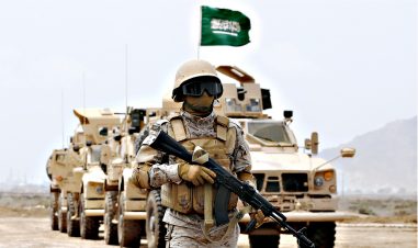 En soldat med våpen står foran en kolonne med bilder med det saudiske flagget på toppen