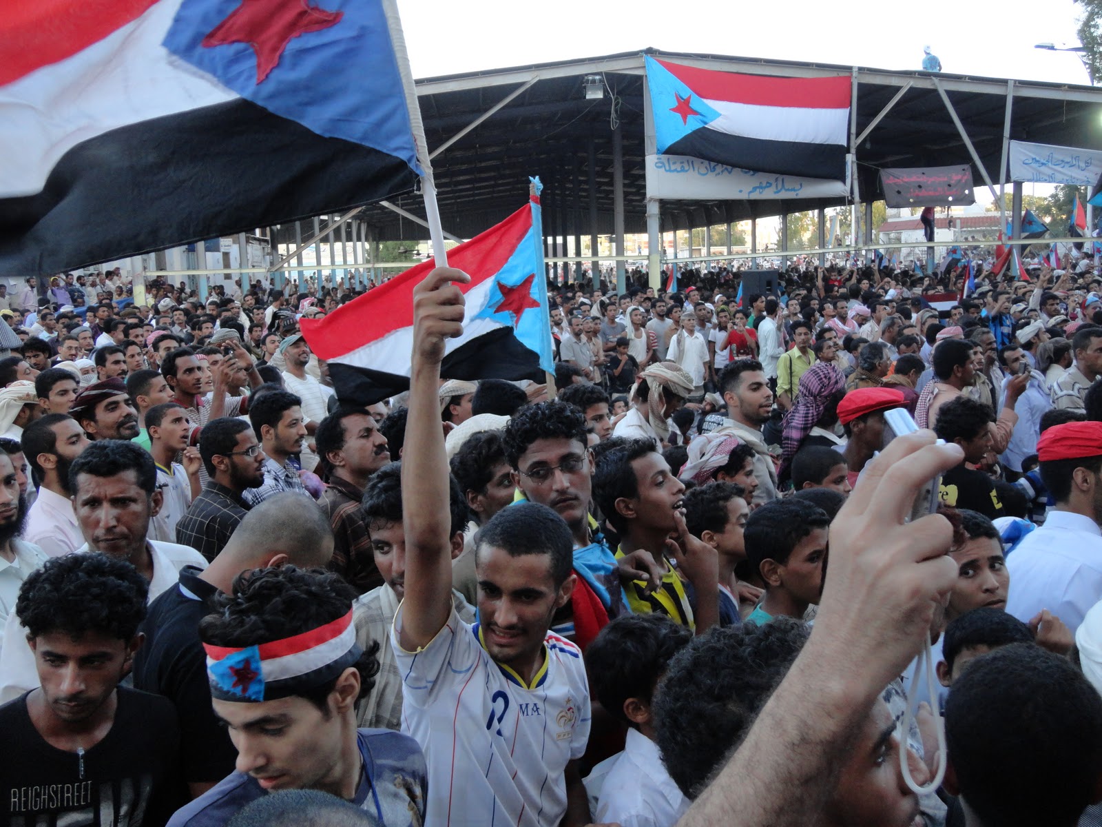 Demonstranter står tett i tett og veiver Jemens flagg