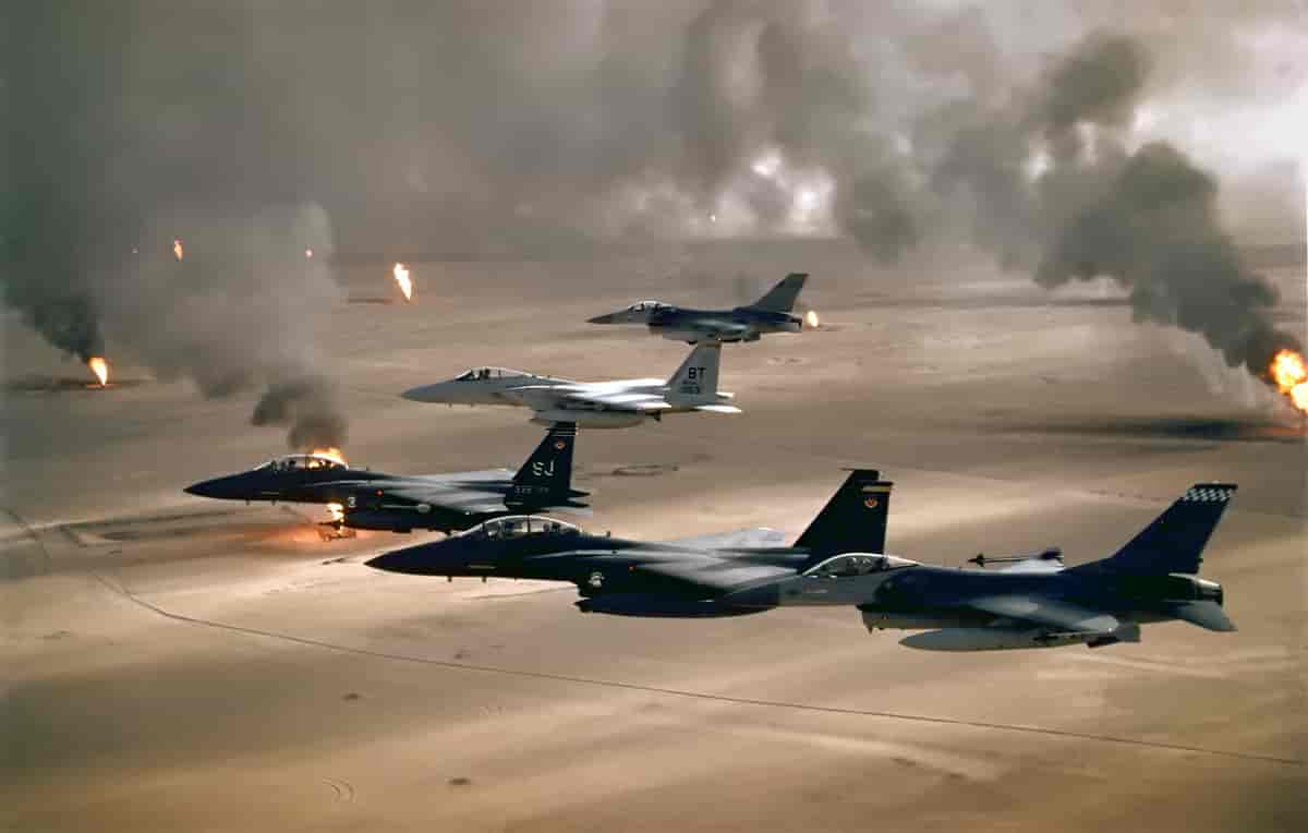 Flere jagerfly over et ørkenområdet. Eksplosjoner og ild ses i bakgrunnen