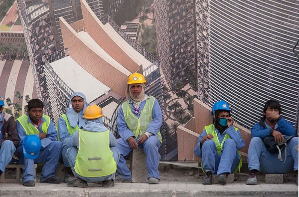 Flere bygningsarbeidere sitter og tar en pause langs en vegg.
