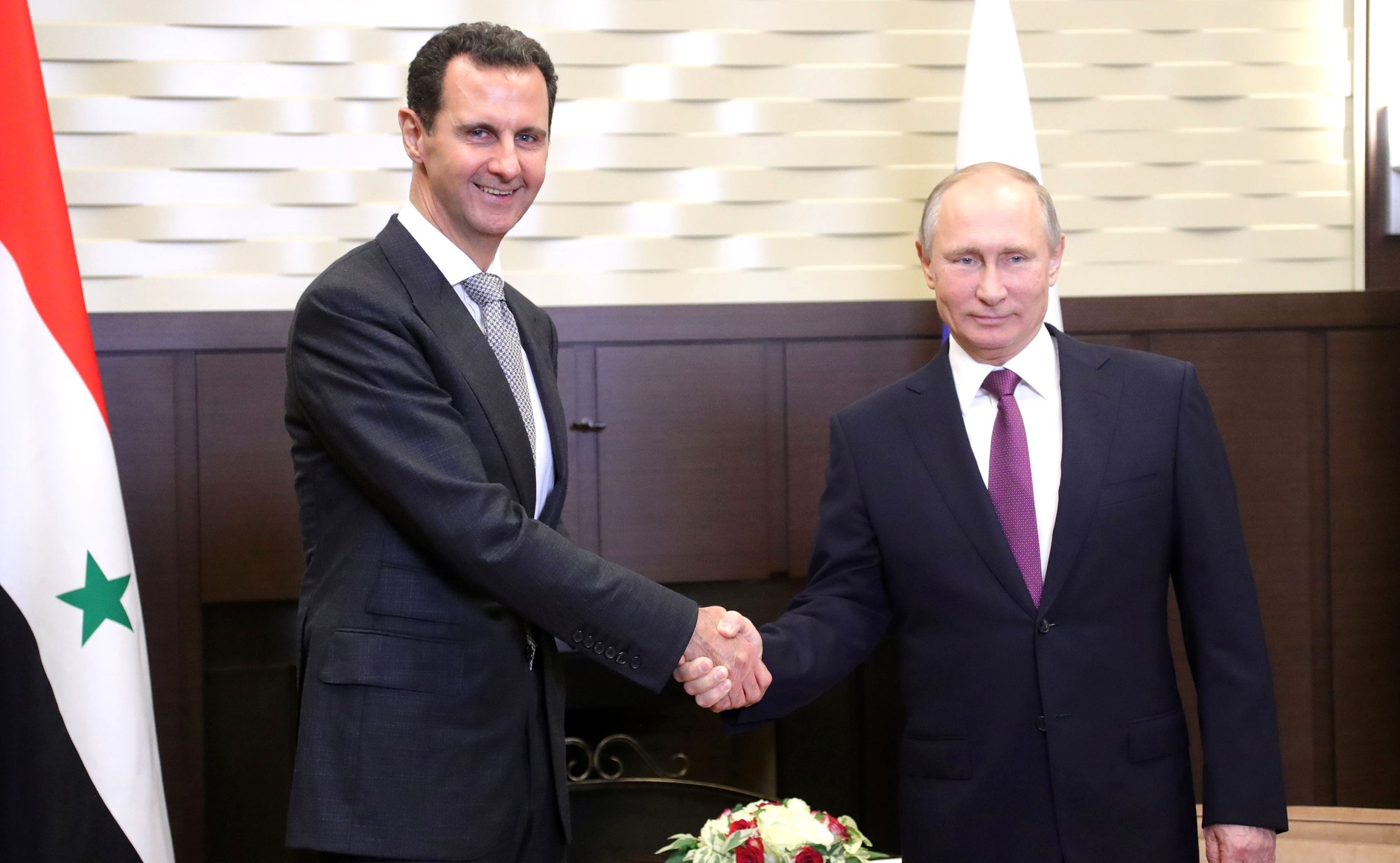 President Assad og President Putin tar hverandre i hendene og smiler til kamera.