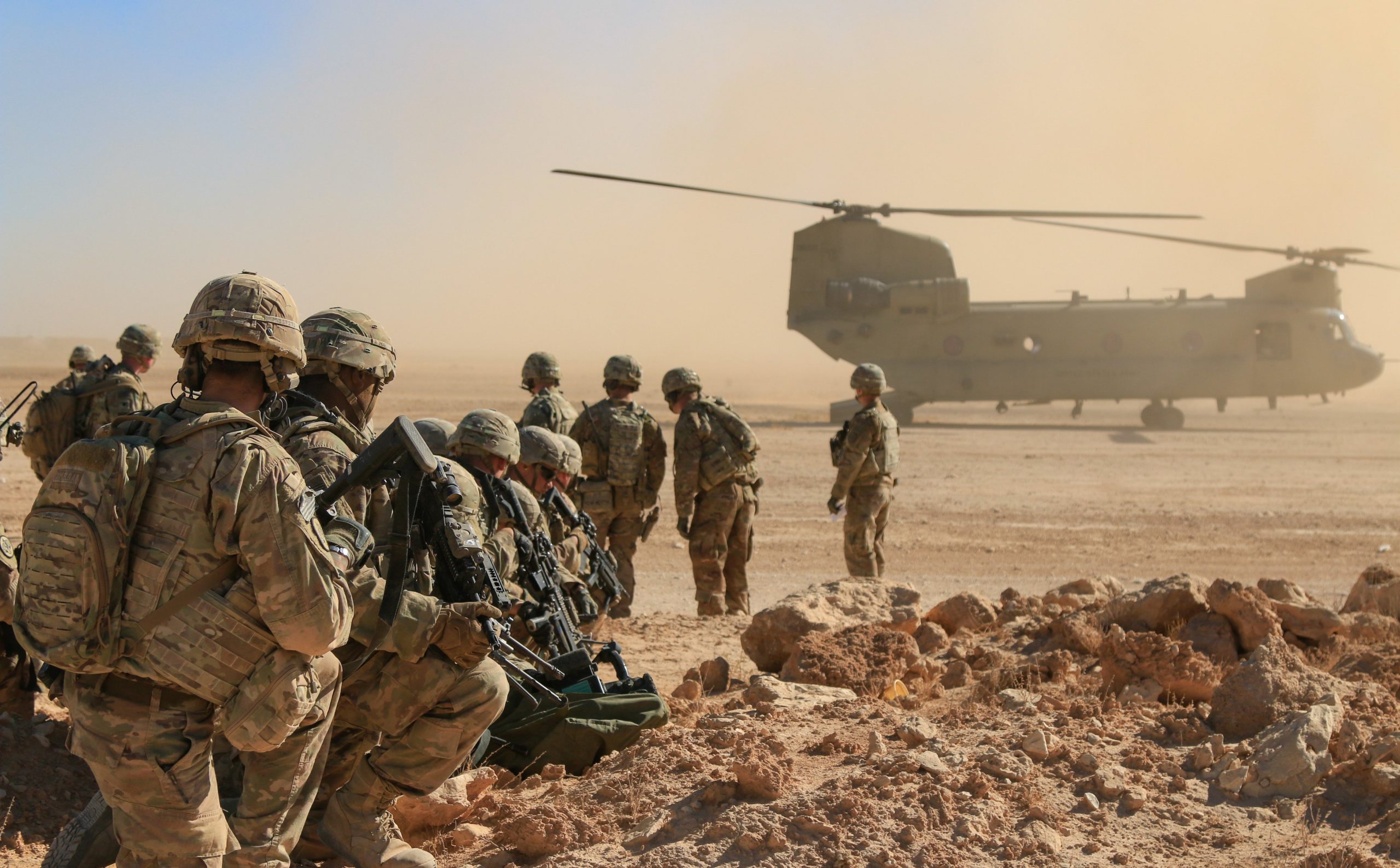 Soldater i sanddekt område med et militært fly i bakgrunnen