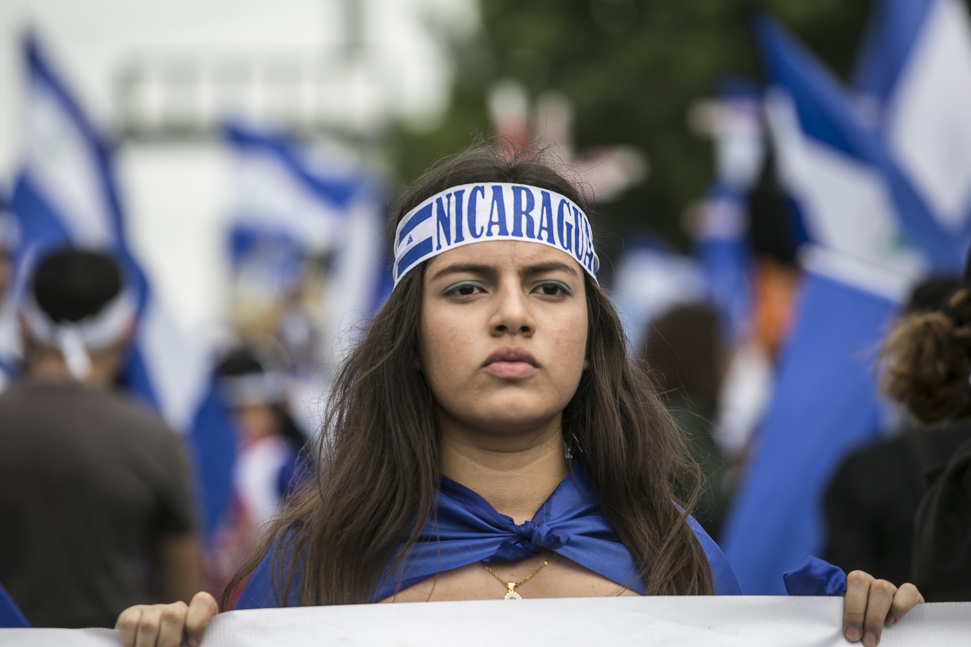 En kvinne går i demonstrasjon. Hun har flagget til Nicaragua rundt kroppen og et pannebånd hvor det står Nicaragua 