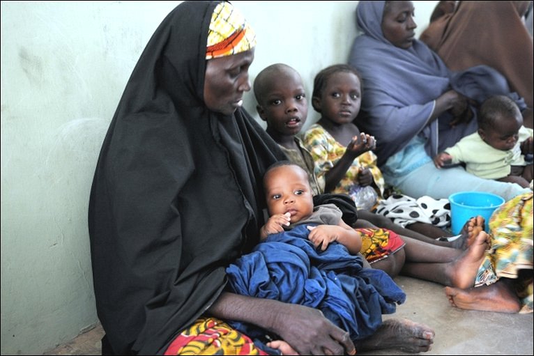 Kvinner og barn sitter langs en vegg i Somalia