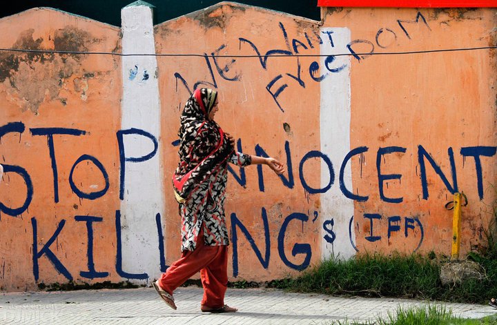 En kvinne går på gaten. På veggen bak henne står det skrevet "Stop Innocent Killings" og "We want freedom"