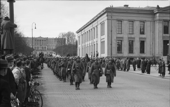 Tyske soldater går nedover en gate. På fortauet står det masse mennesker