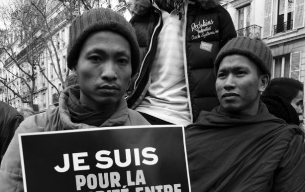 To menn står ute. Den ene holder et skilt hvor det står "Je suis pour la solidarite entre les peuples