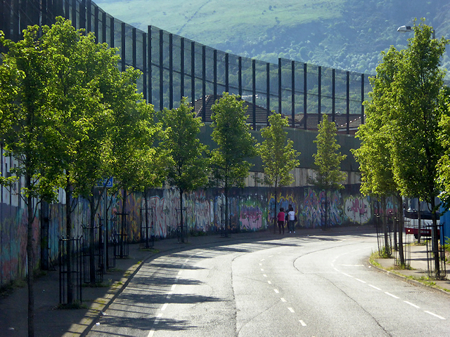 En høy mur langs en vei plantet med trær-