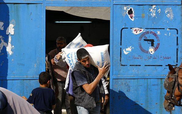 Mann bærer en sekk på ryggen der man kan tyde UNRWAs logo.