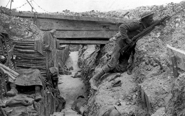 Skyttergrav. Til høyre i bilde en soldat som ligger høyt opp mot kanten med riflen klar. I forgrunnen en soldat som tilsynelatende sover.
