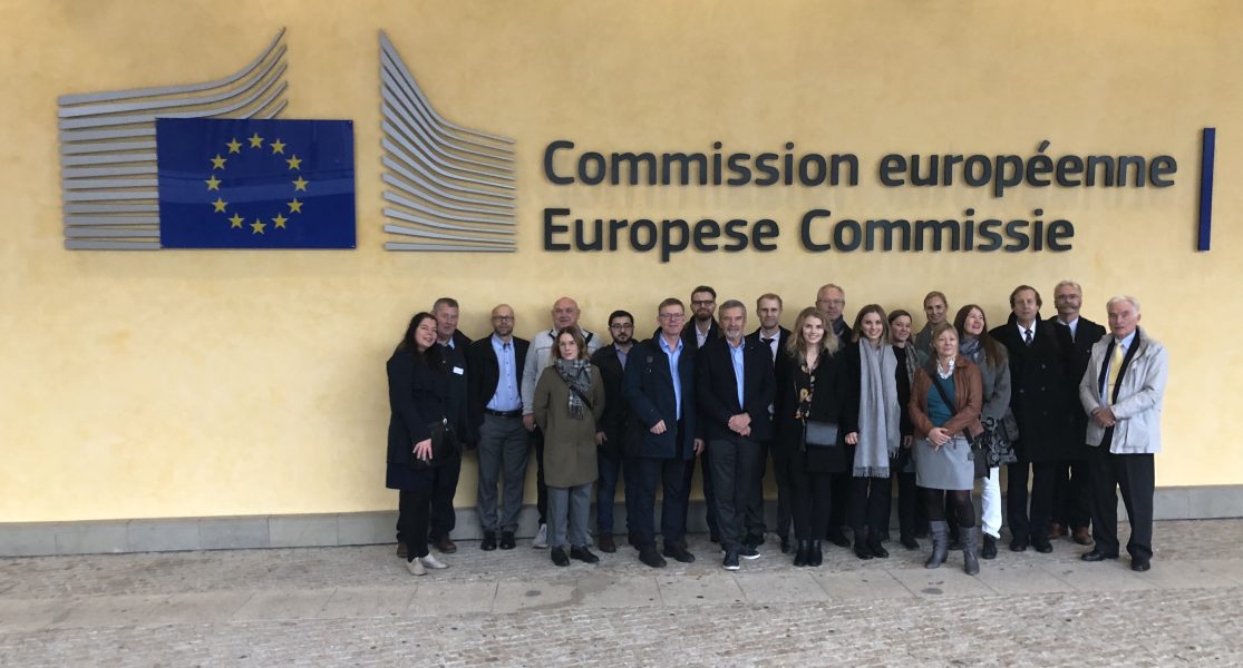 Gruppebilde foran en gull vegg der EU kommisjonens emblem